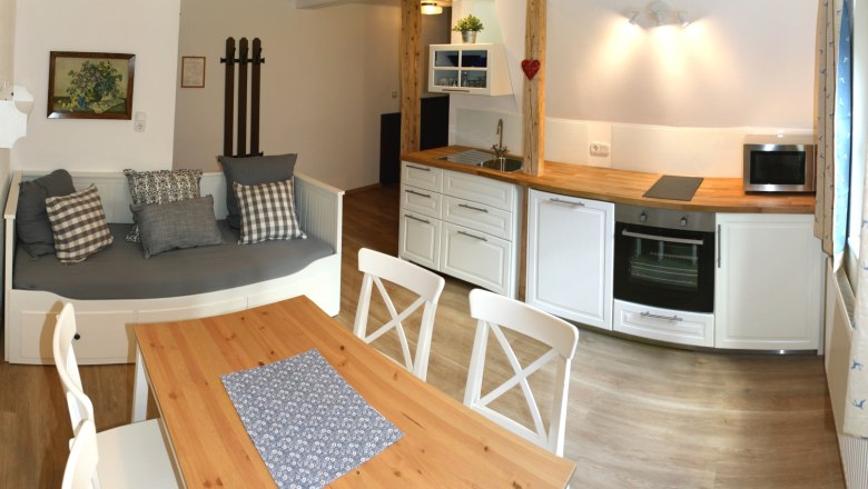 Apartment 1, © Marianne Gschaider Gemütliche Küche mit Holztisch, weißen Stühlen, Sofa und moderner Küchenzeile.