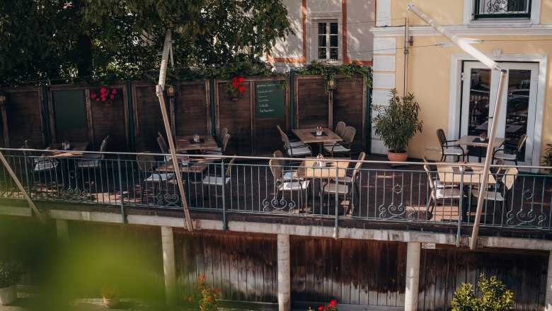 Radfreundliches Wirtshaus am Donauradweg, © Niederösterreich Werbung/Daniela Führer Gemütliche Terrasse eines Cafés mit Holztischen und Stühlen, umgeben von Pflanzen.