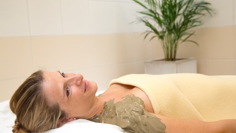 Schwefelschlammpackung, © Badener KurbetriebsgesmbH/Ulz Frau entspannt mit Schwefelschlammpackung auf der Schulter, eingewickelt in eine Decke, im Wellnessbereich mit Pflanze im Hintergrund.