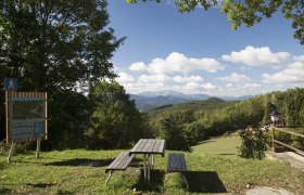 Wanderstartplatz Waxeneckhaus, © Wiener Alpen, Foto: Franz Zwickl Picknicktisch mit Blick auf bewaldete Hügel und Berge, blauer Himmel mit Wolken.