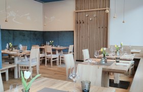 gemütliche Nische, © das GrimmenStein Modernes Restaurant mit Holzmöbeln, gedeckten Tischen, Deckenlampen und blauen Akzenten.