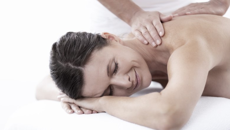 Heilmassage, © NMC Frau erhält eine Rückenmassage und lächelt entspannt.