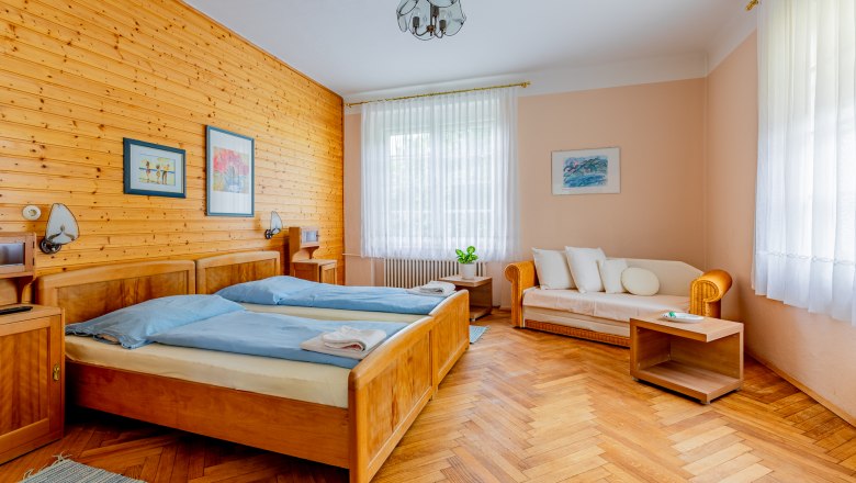 Herrenhaus Woltron, © Wiener Alpen / Christian Kremsl Gemütliches Schlafzimmer mit Holzwänden, zwei Betten, Sofa und Holzboden.