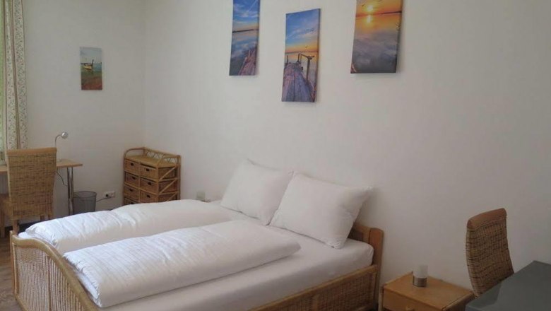 Zimmeransicht, © Casa Topolino Helles Schlafzimmer mit Doppelbett, Rattanmöbeln und Wandbildern.