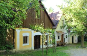 Kellergasse Wolkersdorf, © Weinviertel Tourismus Traditionelle Weinkeller in der Kellergasse von Wolkersdorf, umgeben von grünen Bäumen und Weinreben.
