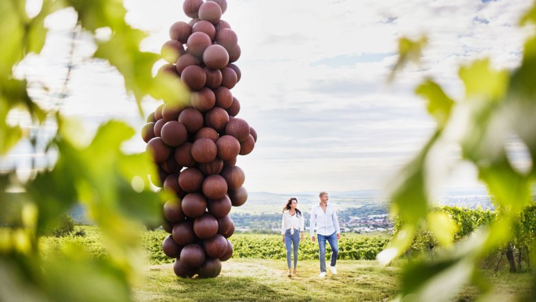 Riesenweintraube entlang des Weinwegs, © © Waldviertel Tourismus, Gerhard Wasserbauer Zwei Personen spazieren neben einer großen Skulptur, der Riesenweintraube, am Weinweg in den Weinbergen.