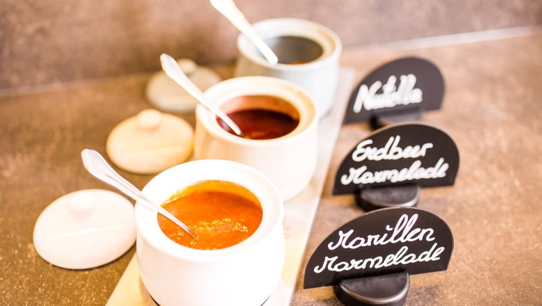 Frühstücksbuffet im Winzerhof Leonhartsberger, © winzerhof leonhartsberger Drei Schalen mit Marmelade und Nutella, beschriftet mit "Marillen Marmelade", "Erdbeer Marmelade" und "Nutella".