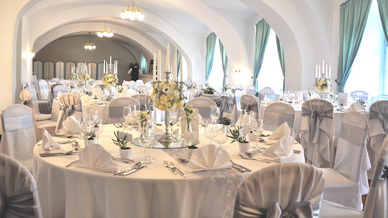 Grosser Saal im Schloss Gloggnitz, © Brentrup Eleganter Bankettsaal mit gedeckten Tischen und weißen Stuhlhussen im Schloss Gloggnitz.