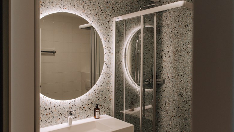 Badezimmer, Comfort HEINhotel vienna airport, © HEINhotel vienna airport Modernes Badezimmer mit beleuchtetem Spiegel und Dusche.