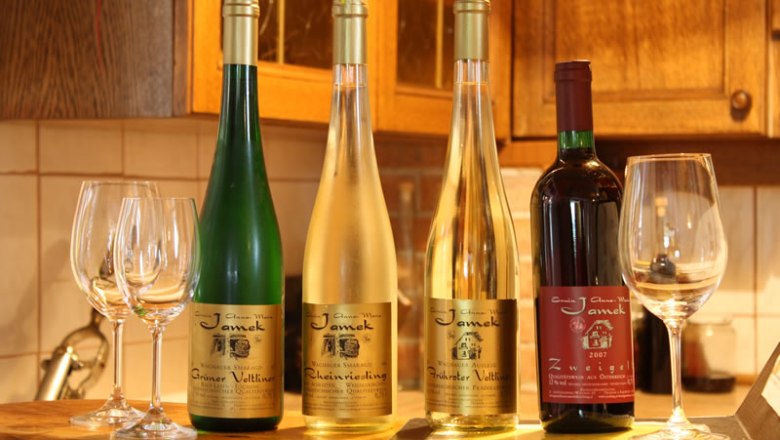 Wein aus eigener Erzeugung, © Jamek Vier Weinflaschen und Gläser auf einem Tisch in einer Küche.