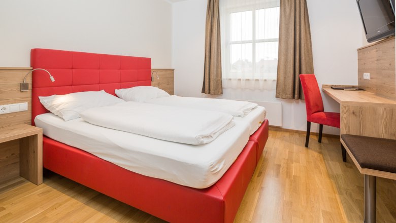 Hotel Unter den Linden 217, © Hotel Unter den Linden Modernes Hotelzimmer mit rotem Bett und Schreibtisch.