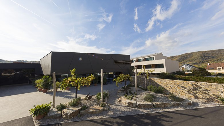 Zufahrt Weinlodge, © Weinlodge Siedler Modernes Gebäude mit Garten und Steinmauer im Vordergrund.