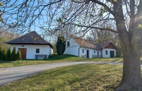 Kellergasse Altruppersdorf, © Vino Versum Poysdorf Weiße Gebäude mit roten Dächern in ländlicher Umgebung, Bäume im Vordergrund.