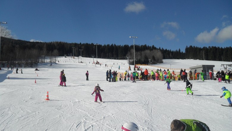 Familienarena, © rosinger Kinder und Erwachsene beim Skifahren auf einer Piste mit blauem Himmel.