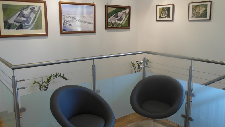 Stiegenaufgang im Lugerhof, © Lugerhof Moderner Innenbereich mit zwei schwarzen Stühlen und einem Glastisch vor einer Wand mit gerahmten Bildern.