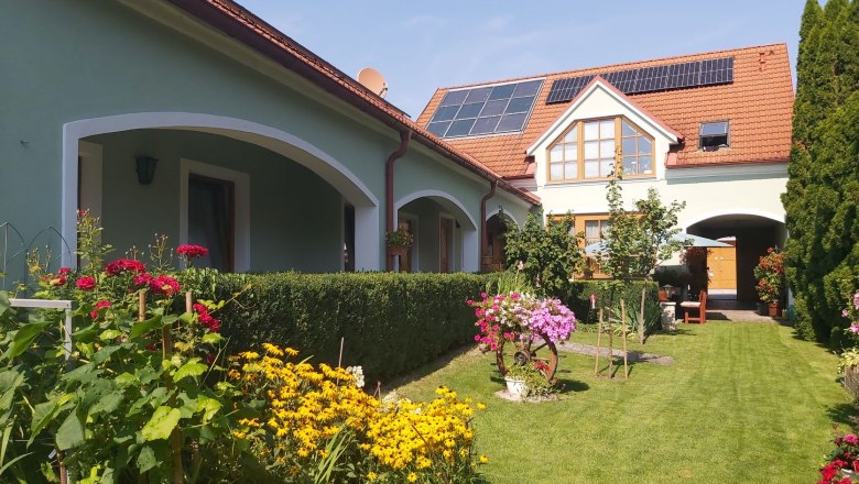 20210813_152903_garten_mittel, © Schwarzinger Ein gepflegter Garten mit bunten Blumen und einem Haus mit Solarpanelen auf dem Dach.