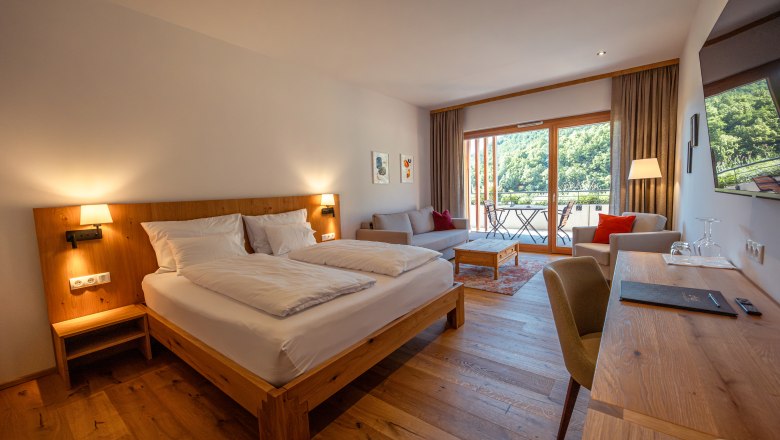 Weinhotel Nigl, © Niederösterreich Werbung / Maximilian Pawlikowsky Ein modernes Hotelzimmer mit Doppelbett, Sofa, Schreibtisch und Balkon mit Blick auf grüne Hügel.