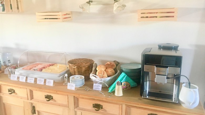 Frühstücksbuffet, © Fam. Ritz Frühstücksbuffet mit Aufschnitt, Brötchen und Kaffeemaschine auf einem Holztisch.