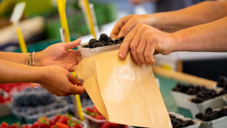 Wochenmarkt Korneuburg, © Markjan.photography Nahaufnahme von Händen, die auf einem Markt Beeren in eine Papiertüte übergeben.