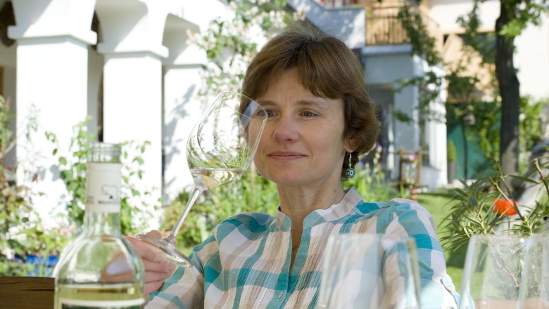 Gastgeberin, © Michael Himml Frau mit Weinglas im Garten, Flasche im Vordergrund.
