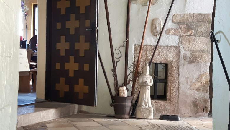 In der Burg, © www.burg-grimmenstein.at Innenansicht einer Burg mit Waffen, einem Wildschweinkopf und einer Statue.