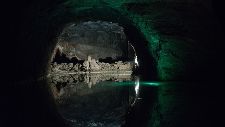 Blauer See, © Seegrotte Dunkle Höhle mit Wasser und Felsformationen, beleuchtet von grünlichem Licht.