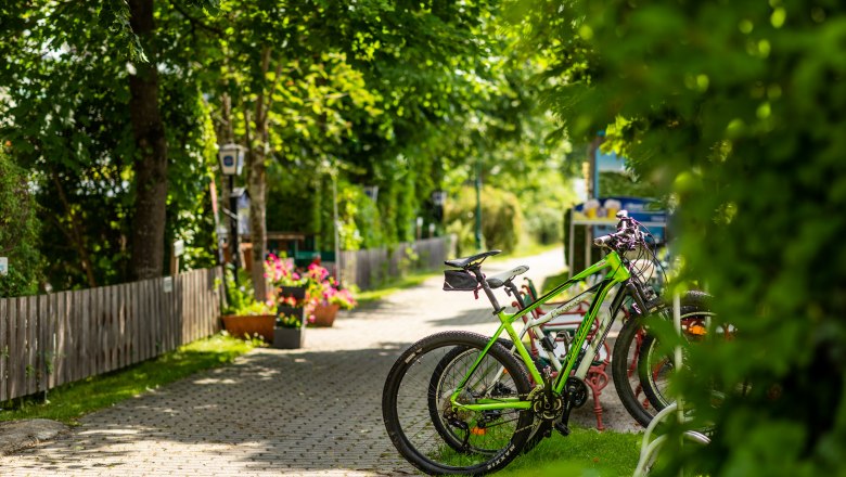 Radparkplatz beim Gasthof St. Wolfgang, © Wiener Alpen/Martin Fülöp Fahrräder geparkt auf einem Radparkplatz bei einem Gasthof, umgeben von grünen Bäumen und Blumen.