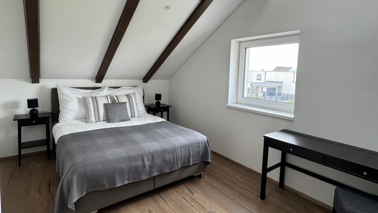 Schlafzimmer, © Juwel am Stadtrand Modernes Schlafzimmer mit Holzbalkendecke, Doppelbett, Holzboden und Fenster.