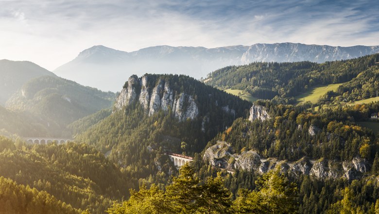 "20-Schilling-Blick", © NOEW - Liebert Panoramablick auf eine Berglandschaft mit Viadukt und bewaldeten Hügeln.