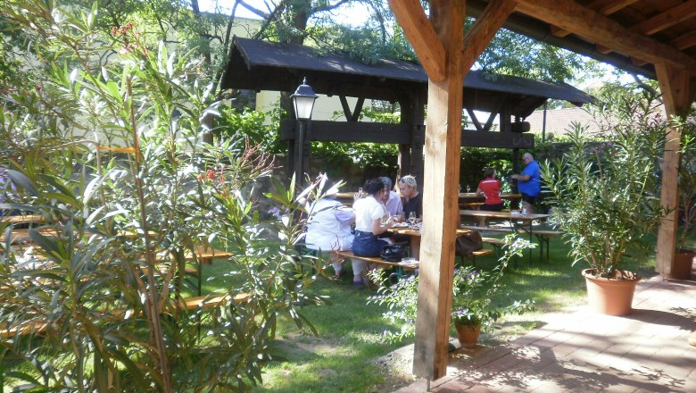 Heurigenbetrieb Lager, © Lager Garten eines Heurigenbetriebs mit Holztischen und Pflanzen.