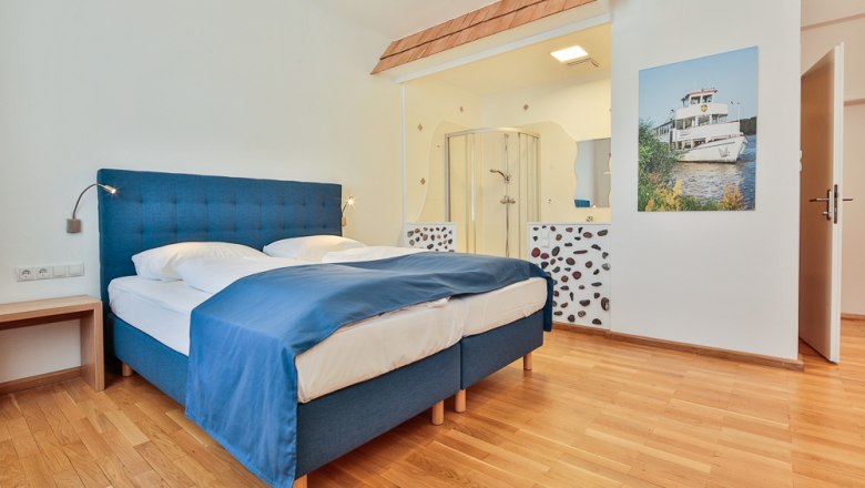 Hotel Unter den Linden Zimmer 204, © Hotel Unter den Linden Hotelzimmer mit blauem Bett, Holzboden und offener Dusche.