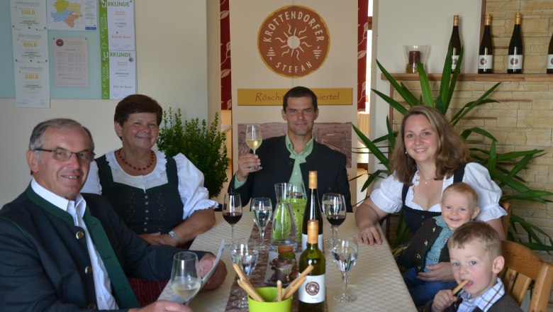 Familie Krottendorfer, © Familie Krottendorfer Familie in traditioneller Kleidung sitzt an einem Tisch mit Wein und Gläsern.