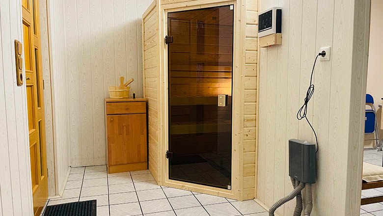 sauna, © Angelika Burger Innenansicht eines Saunaraums mit Holzwänden, einer Glastür und einem kleinen Holzschrank.
