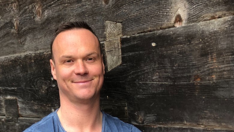 Herwald Hauleitner, © Hauleitner Mann in blauem T-Shirt vor Holzwand.