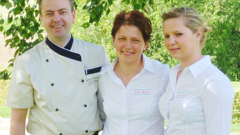 Restaurant Hettegger, © MG Rfd Drei Personen in Restaurantuniformen stehen lächelnd unter einem Baum.