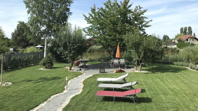 Garten, © Familie Mokesch Ein gepflegter Garten mit Rasen, Bäumen, Sonnenliegen und einem Tisch mit Sonnenschirm.