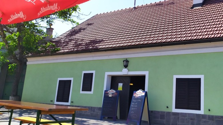 Heuriger Maier Außenansicht, © Weinbau Maier Außenansicht eines traditionellen Heurigen mit grünem Anstrich und roten Dachziegeln. Vor dem Gebäude stehen Holzbänke und ein roter Sonnenschirm.