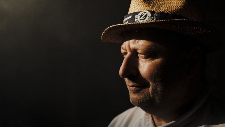 Grill-Weltmeister Adi Bittermann, © Niederösterreich Werbung/Michael Reidinger Porträt eines Mannes mit Strohhut im Profil, im Schatten stehend.