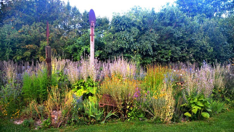 staudenbeet_klein_kontrast_c_familie-mahr, © Familie Mahr Ein buntes Staudenbeet mit verschiedenen Blumen und Pflanzen vor einem Holzzaun und Bäumen.