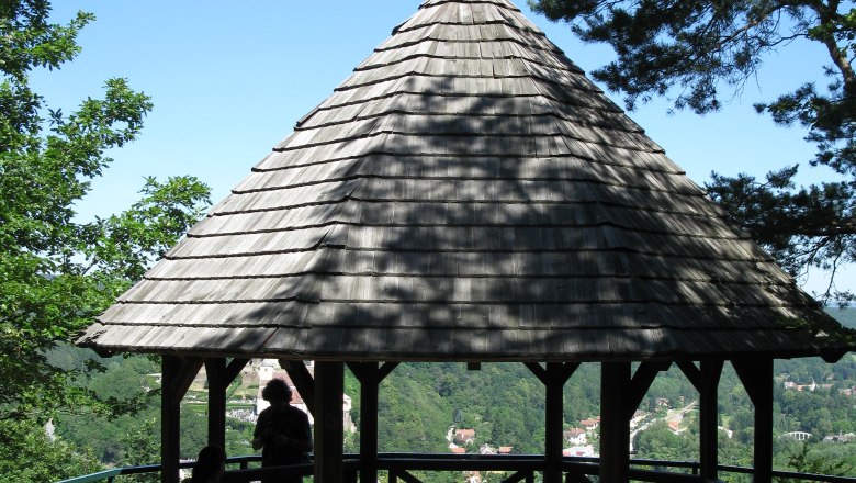 Hamerlingwarte Gars, © Wachauer Ein hölzerner Pavillon mit spitzem Dach auf einem Hügel, umgeben von Bäumen, mit Blick auf eine grüne Landschaft.