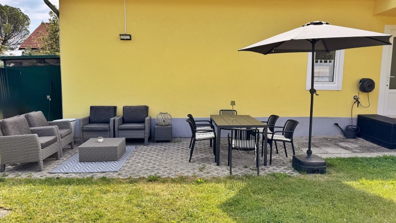 Terrasse, © Christoph Menhofer Terrasse mit gelber Hauswand, grauen Sitzmöbeln, Esstisch, Stühlen und Sonnenschirm.