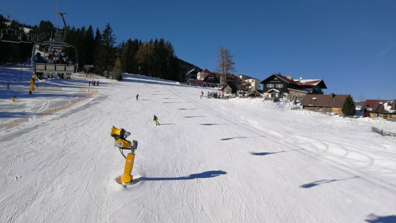 Schipiste Mönichkirchen, © Józef Swierkot Skifahrer auf einer sonnigen Piste in Mönichkirchen mit Sessellift und Schneekanonen.