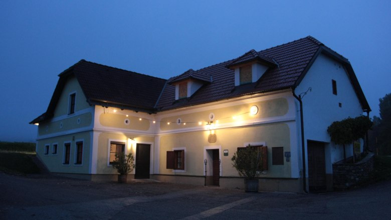 Fam. Ortmann, © z.V.g. Fam. Ortmann Ein traditionelles, beleuchtetes Haus mit gelber Fassade und roten Dachziegeln in der Dämmerung.