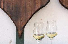 Weingläser, © Weinviertel Tourismus / Doris Schwarz-König Zwei Weingläser mit Weißwein auf einem Holztisch vor einer herzförmigen Holzdekoration.