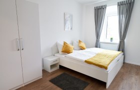 Doppelzimmer, © Eugenia Husti Modernes Doppelzimmer mit weißem Bett, gelben Kissen und grauen Vorhängen.