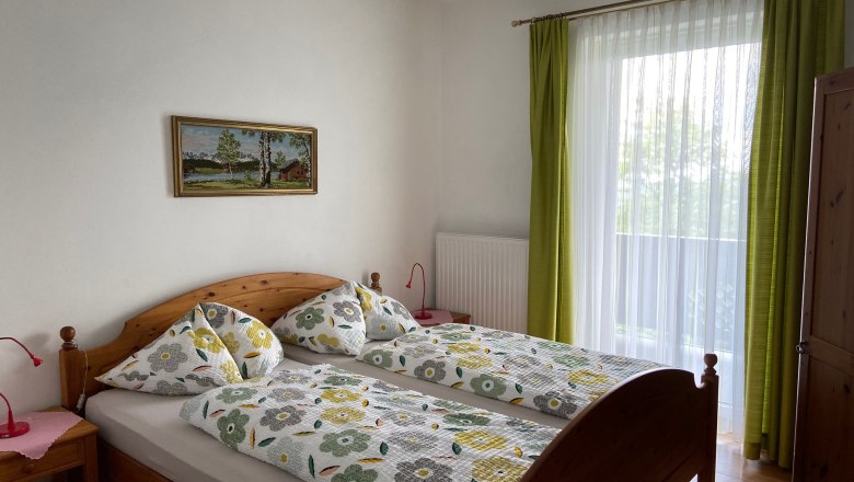 Doppelzimmer, © Wiener Alpen Ein gemütliches Doppelzimmer mit Holzmöbeln, einem großen Fenster mit grünen Vorhängen und einem Landschaftsbild an der Wand.