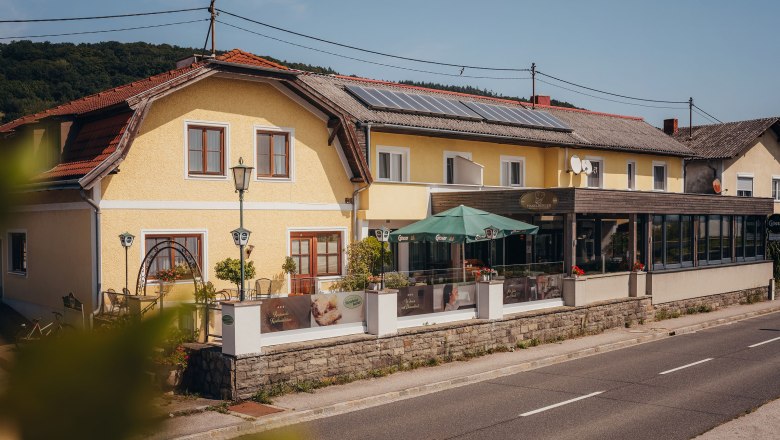 Wirtshaus am Donauradweg, © Niederösterreich Werbung/Daniela Führer Gelbes Gasthaus mit Terrasse und Sonnenschirmen an einer Landstraße.