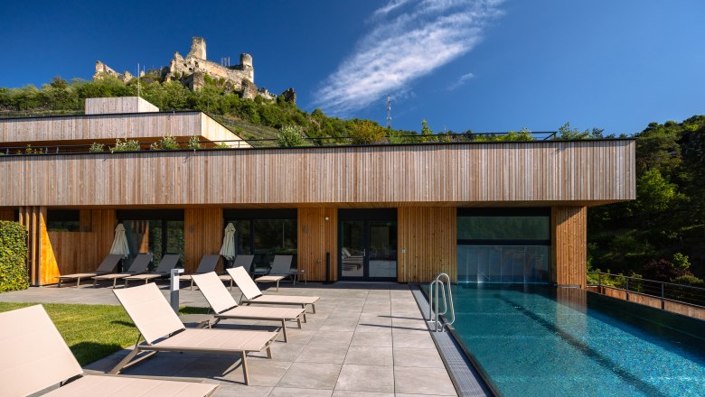 Weinhotel Nigl, © Niederösterreich Werbung / Maximilian Pawlikowsky Modernes Hotel mit Pool und Liegestühlen, Burg im Hintergrund.