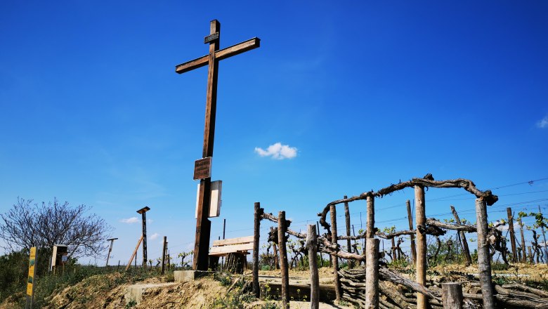 Freiheitskreuz in Haugsdorf, © Weinstraße Weinviertel Holzkreuz auf einem Hügel mit Weinreben und blauem Himmel im Hintergrund.