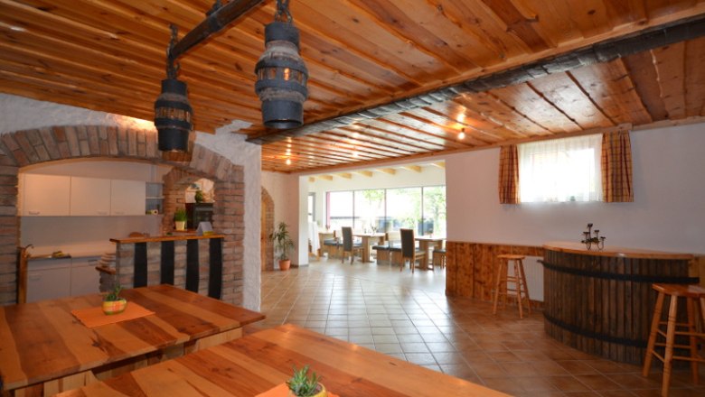 Stüberl - Winzerhof Stauffer, © Winzerhof Stauffer Innenansicht eines rustikalen Gastraums mit Holztischen und -decken, Barbereich und großen Fenstern.